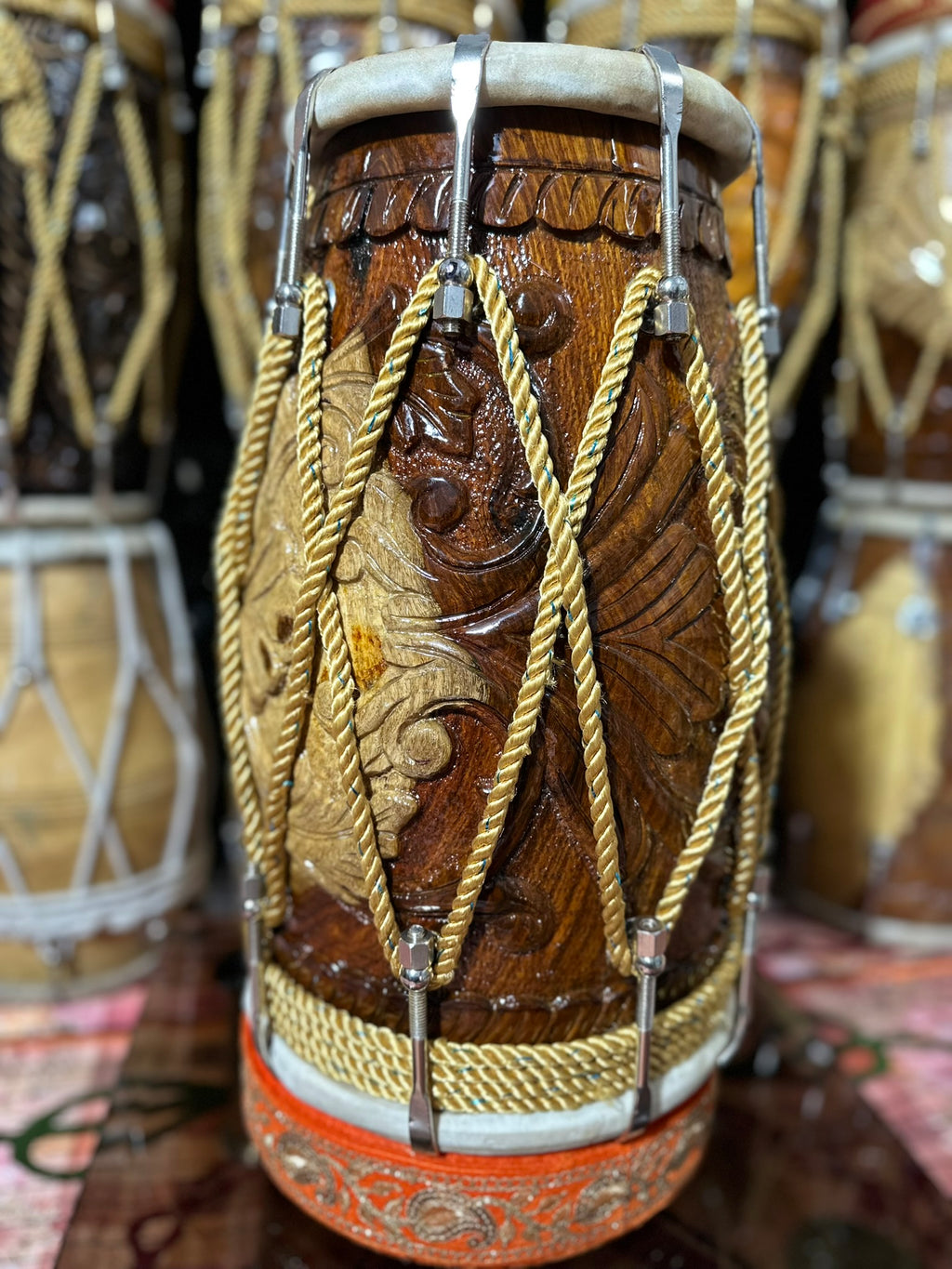 Decorative drum with intricate carvings and gold strings, surrounded by similar drums.